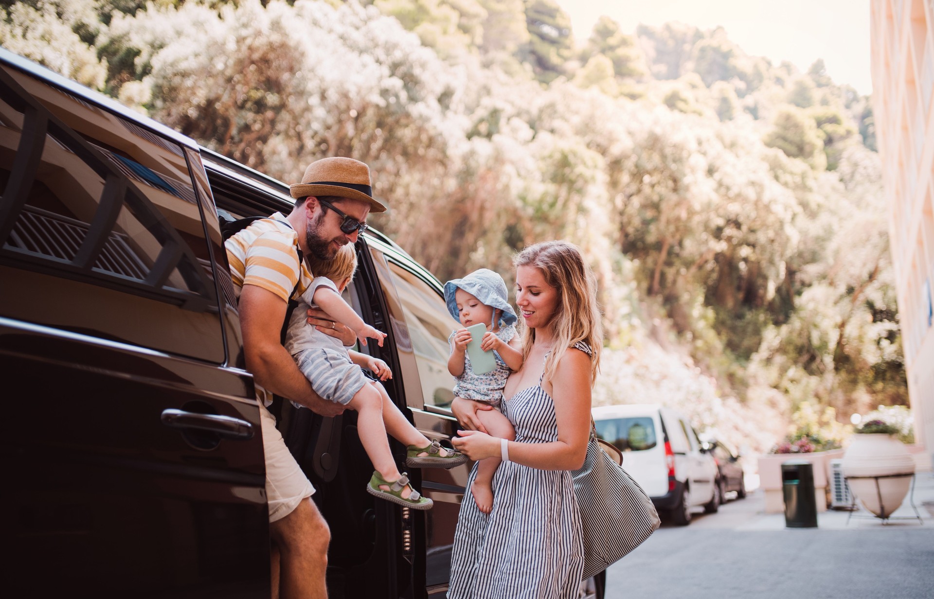 A young family with two toddler children getting out of taxi on summer holiday.