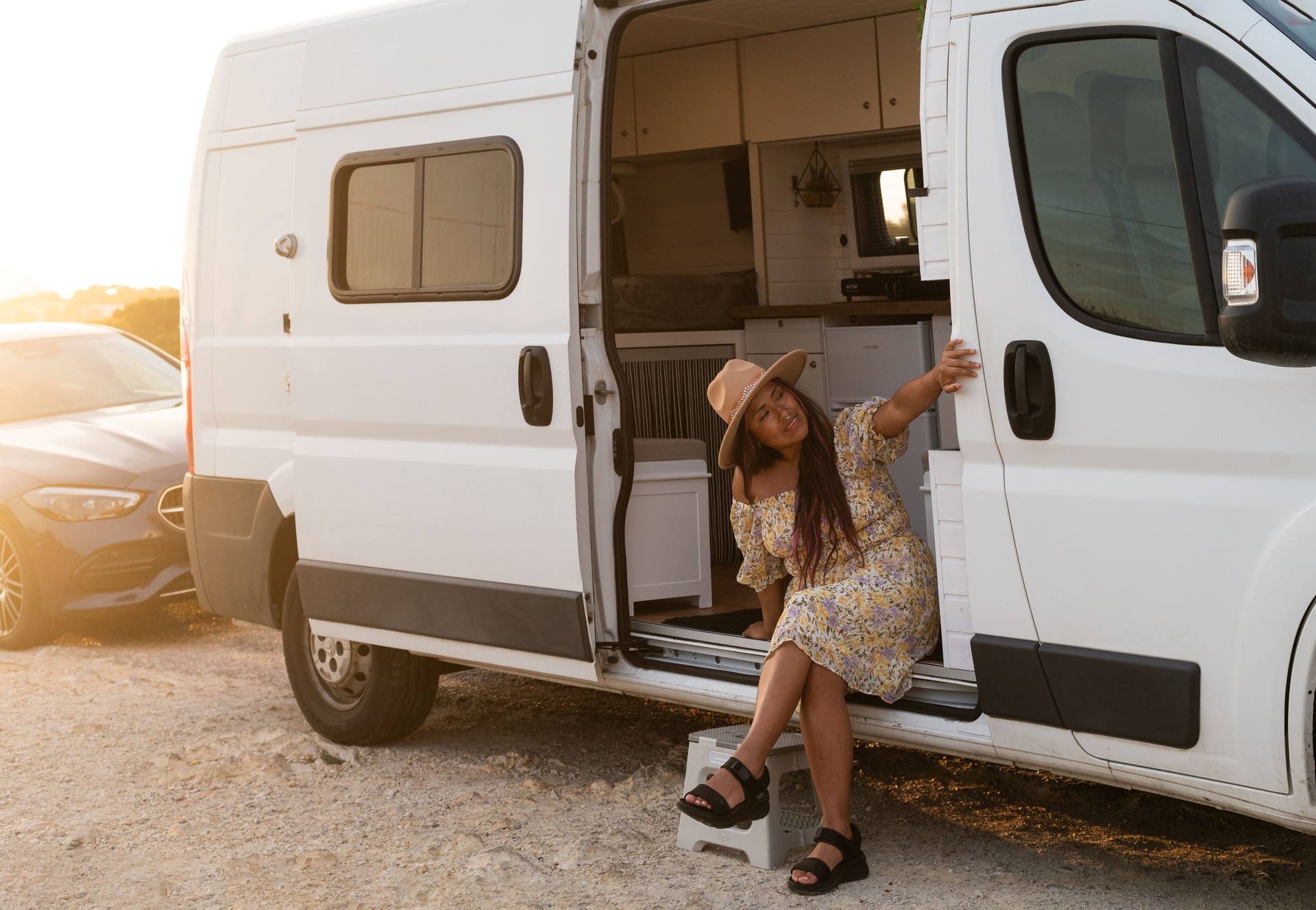Young woman sitting at camper van door enjoying sunset during road trip